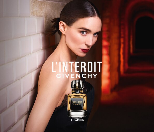L&apos;Interdit Givenchy Le Parfum – elegáns nő fehér csempés háttér előtt, vörös boltívvel és parfüm üveggel az előtérben