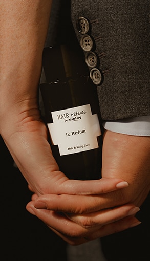 Hair Rituel by Sisley Le Parfum fekete üveg kézben, elegáns öltöny részleteivel, luxus haj- és fejbőrápoló illat.