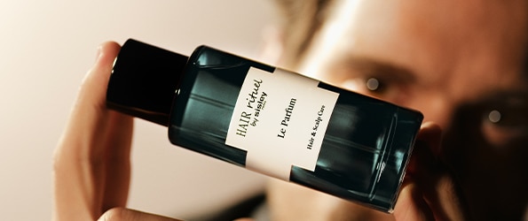 Hair Rituel by Sisley Le Parfum luxus haj- és fejbőrápoló illat fekete üvegben, kézben tartva elegáns megvilágításban.